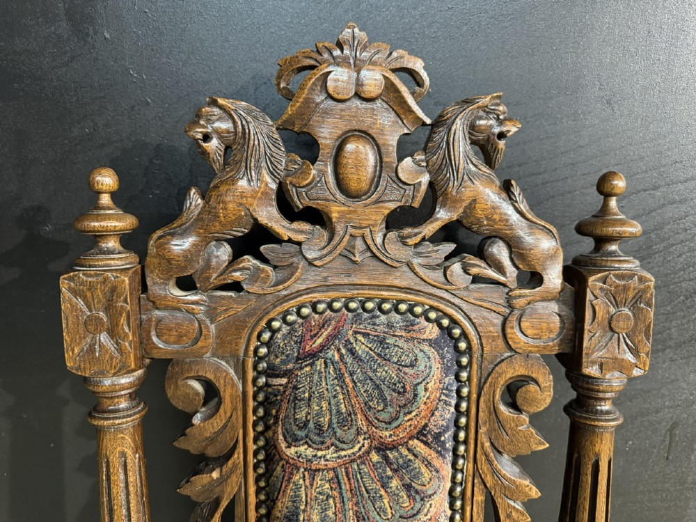 A set of eight high-backed dark oak dining chairs featuring carved lion crests and tapestry fabric upholstery. View VI