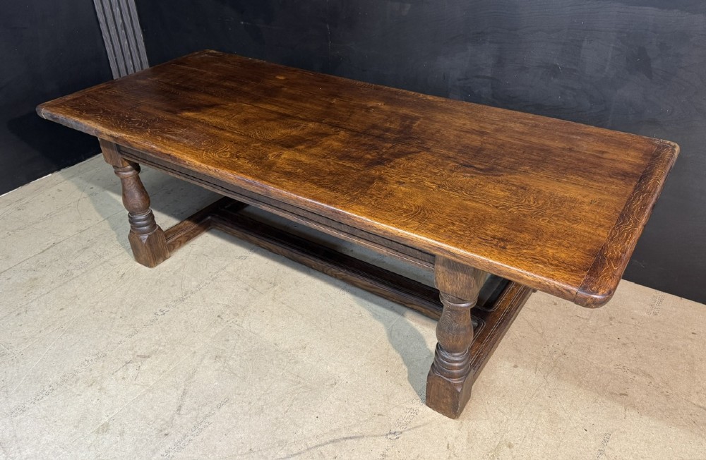 A long and deep solid dark oak farmhouse dining table featuring a plank top, moulded apron, and thick turned baluster legs joined by a floor-level stretcher. View IV