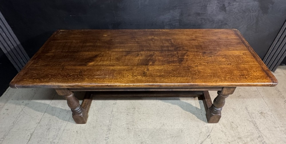 A long and deep solid dark oak farmhouse dining table featuring a plank top, moulded apron, and thick turned baluster legs joined by a floor-level stretcher. View VI