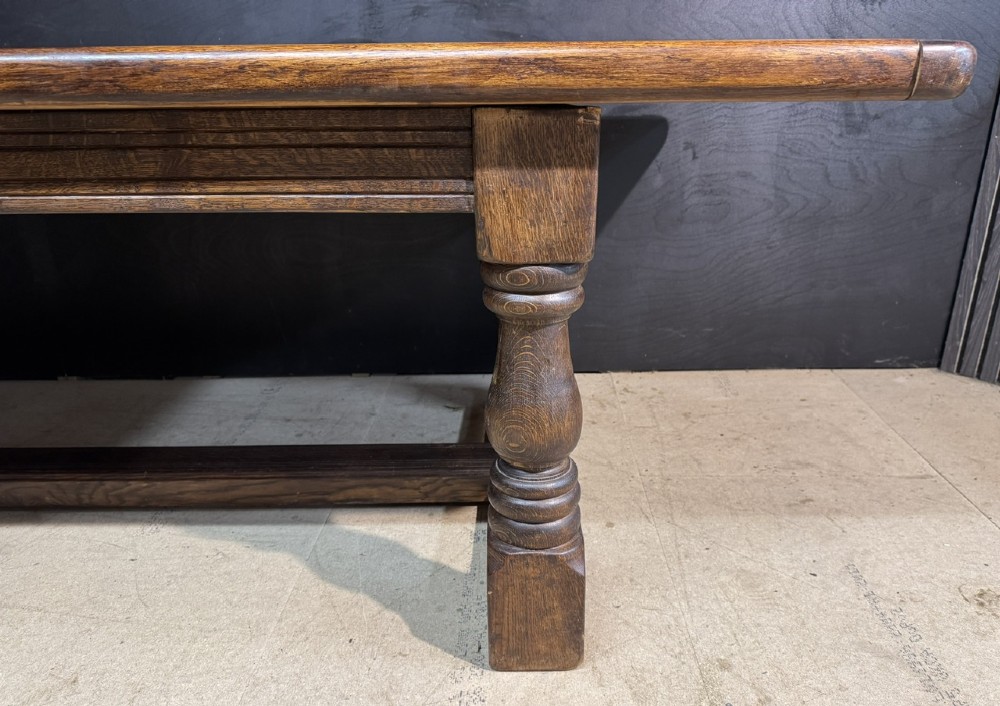 A long and deep solid dark oak farmhouse dining table featuring a plank top, moulded apron, and thick turned baluster legs joined by a floor-level stretcher. View VII