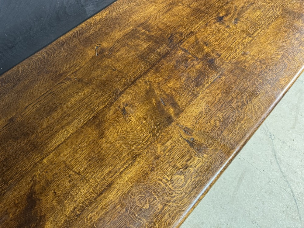 A long and deep solid dark oak farmhouse dining table featuring a plank top, moulded apron, and thick turned baluster legs joined by a floor-level stretcher. View X