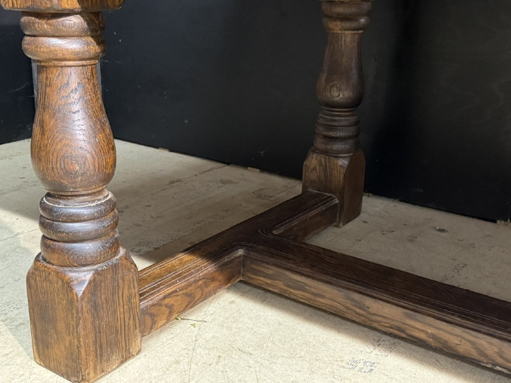 A long and deep solid dark oak farmhouse dining table featuring a plank top, moulded apron, and thick turned baluster legs joined by a floor-level stretcher. View XII