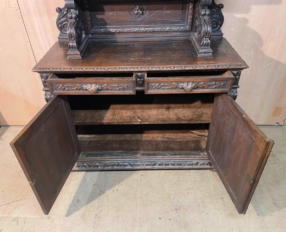 A dark oak French hunting sideboard featuring a carved stag head top pediment, open middle shelves, and lower cabinet doors decorated with carved game birds. View III