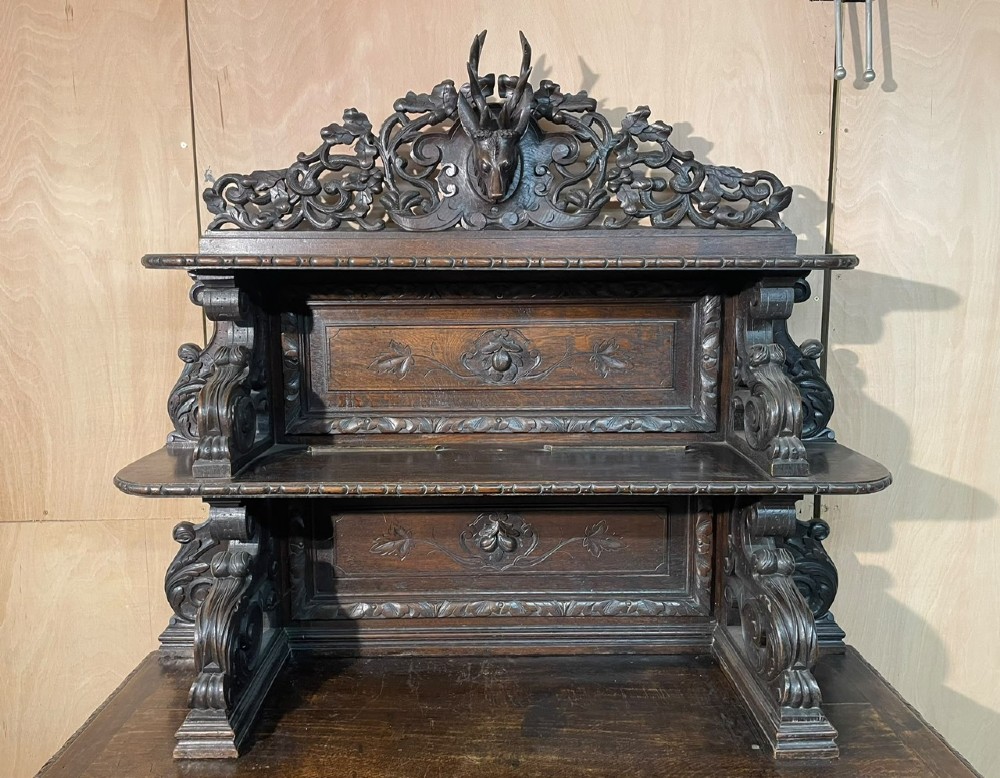 A dark oak French hunting sideboard featuring a carved stag head top pediment, open middle shelves, and lower cabinet doors decorated with carved game birds. View V