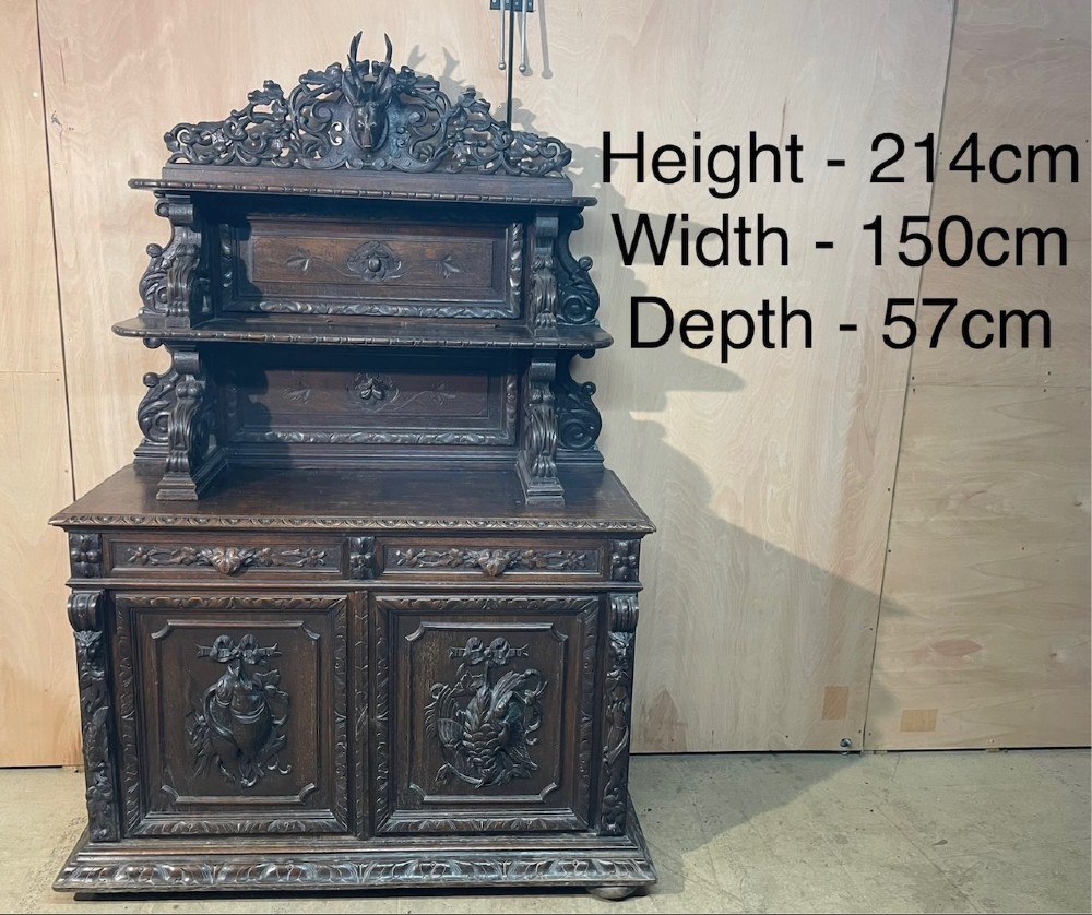 A dark oak French hunting sideboard featuring a carved stag head top pediment, open middle shelves, and lower cabinet doors decorated with carved game birds. View X