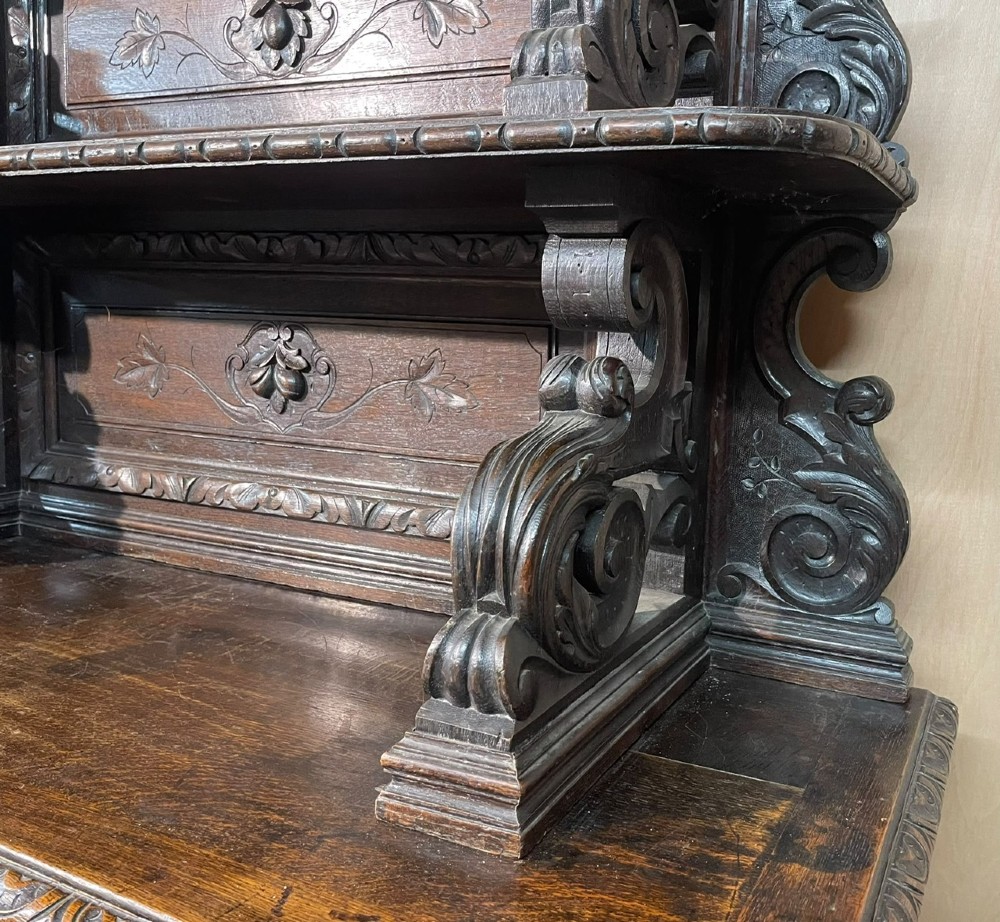 A dark oak French hunting sideboard featuring a carved stag head top pediment, open middle shelves, and lower cabinet doors decorated with carved game birds. View XIII