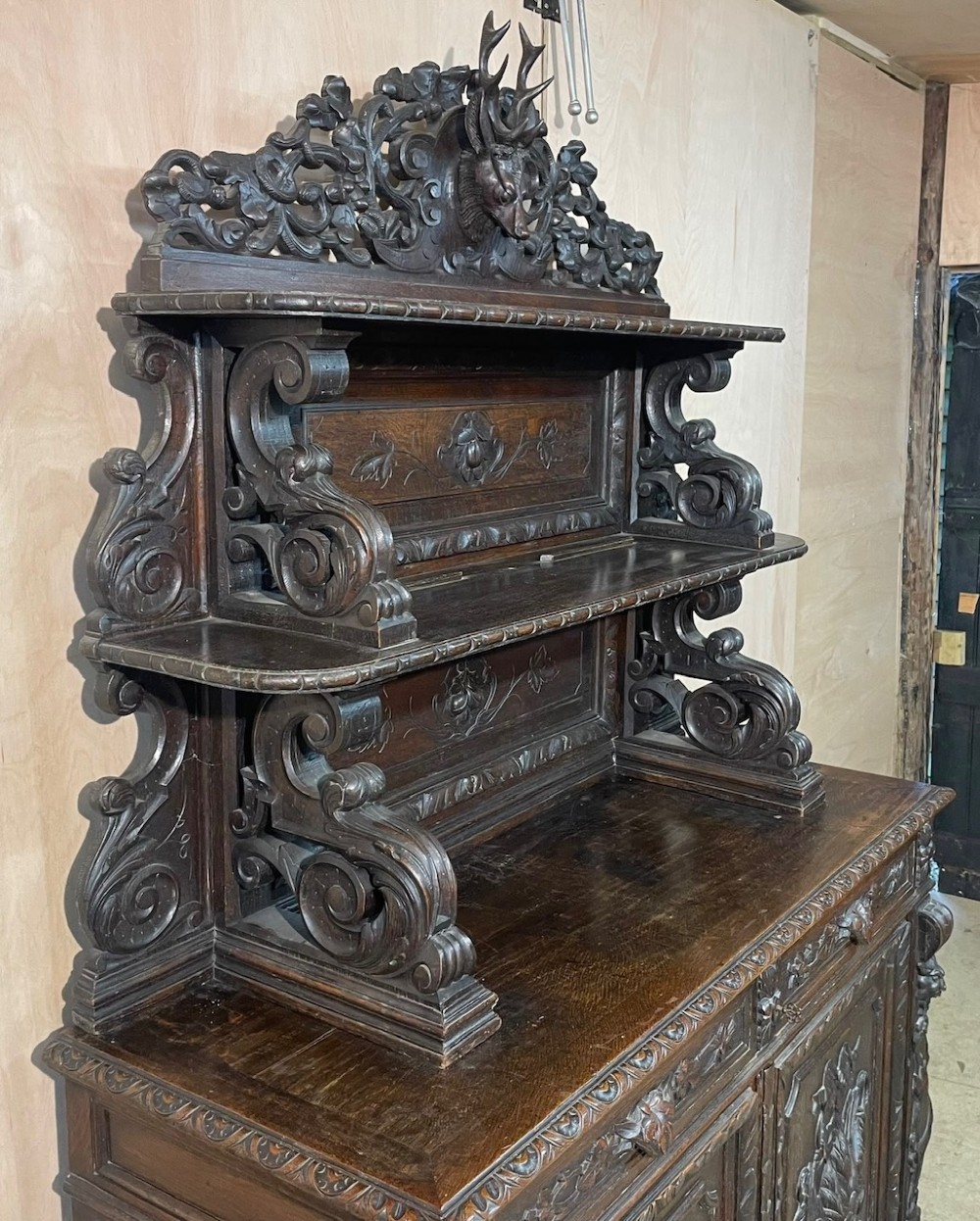 A dark oak French hunting sideboard featuring a carved stag head top pediment, open middle shelves, and lower cabinet doors decorated with carved game birds. View XV