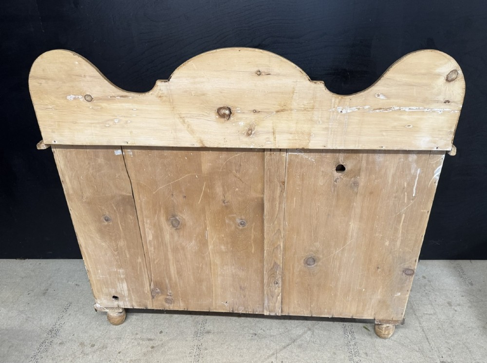 A small antique pine dresser base featuring three drawers on the left, a single panelled cupboard on the right, wooden knobs, turned bun feet, and a shaped back gallery shelf. View VIII