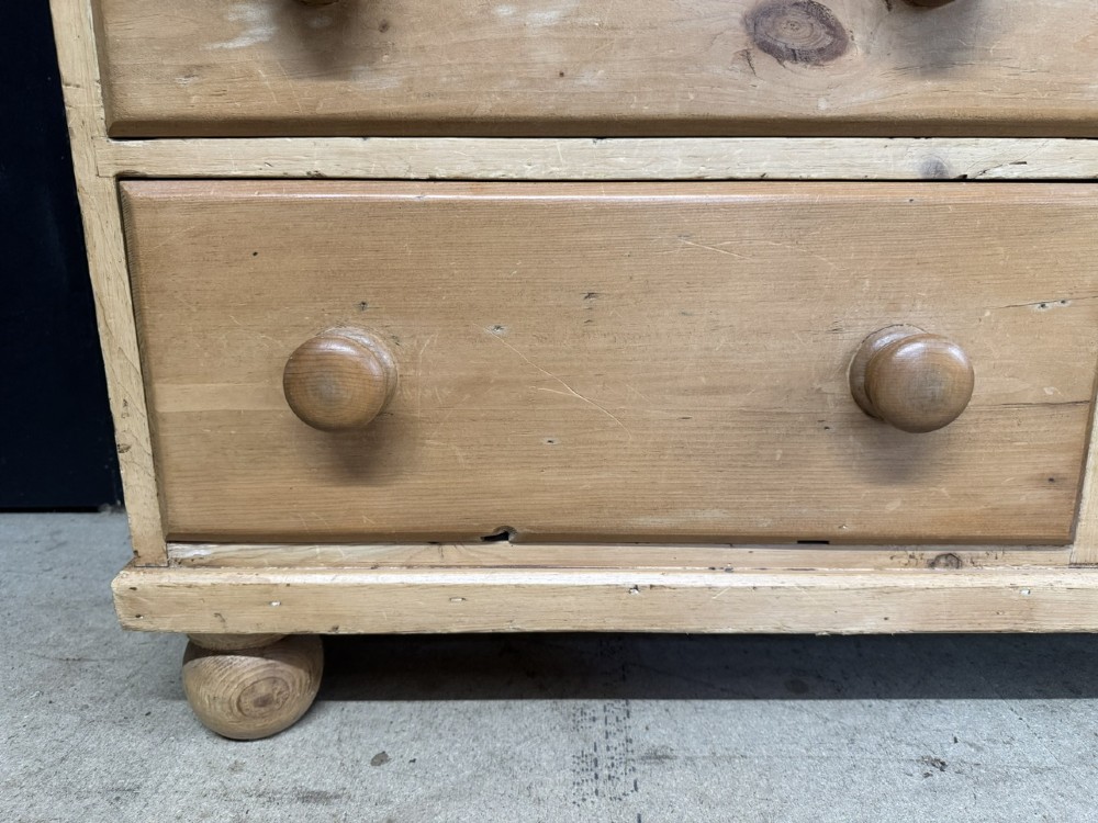 A small antique pine dresser base featuring three drawers on the left, a single panelled cupboard on the right, wooden knobs, turned bun feet, and a shaped back gallery shelf. View IX