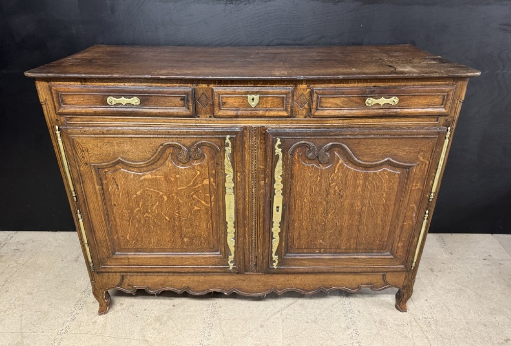 An 18th-century French provincial oak buffet featuring three top drawers above two carved panel doors with brass hardware.