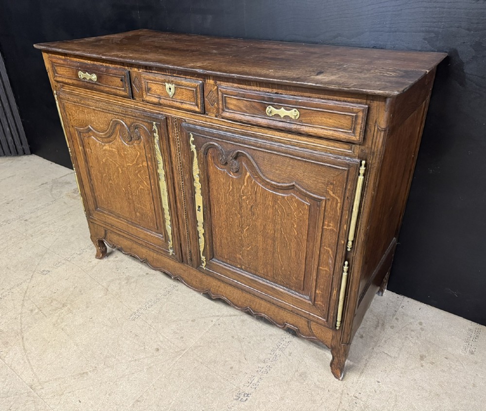 An 18th-century French provincial oak buffet featuring three top drawers above two carved panel doors with brass hardware. View IV