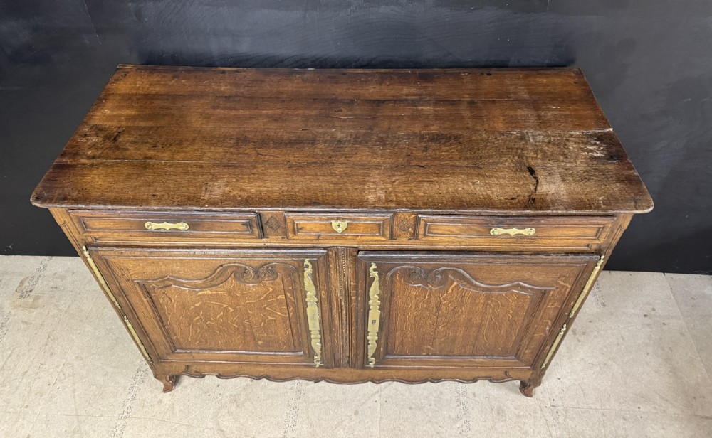 An 18th-century French provincial oak buffet featuring three top drawers above two carved panel doors with brass hardware. View VII