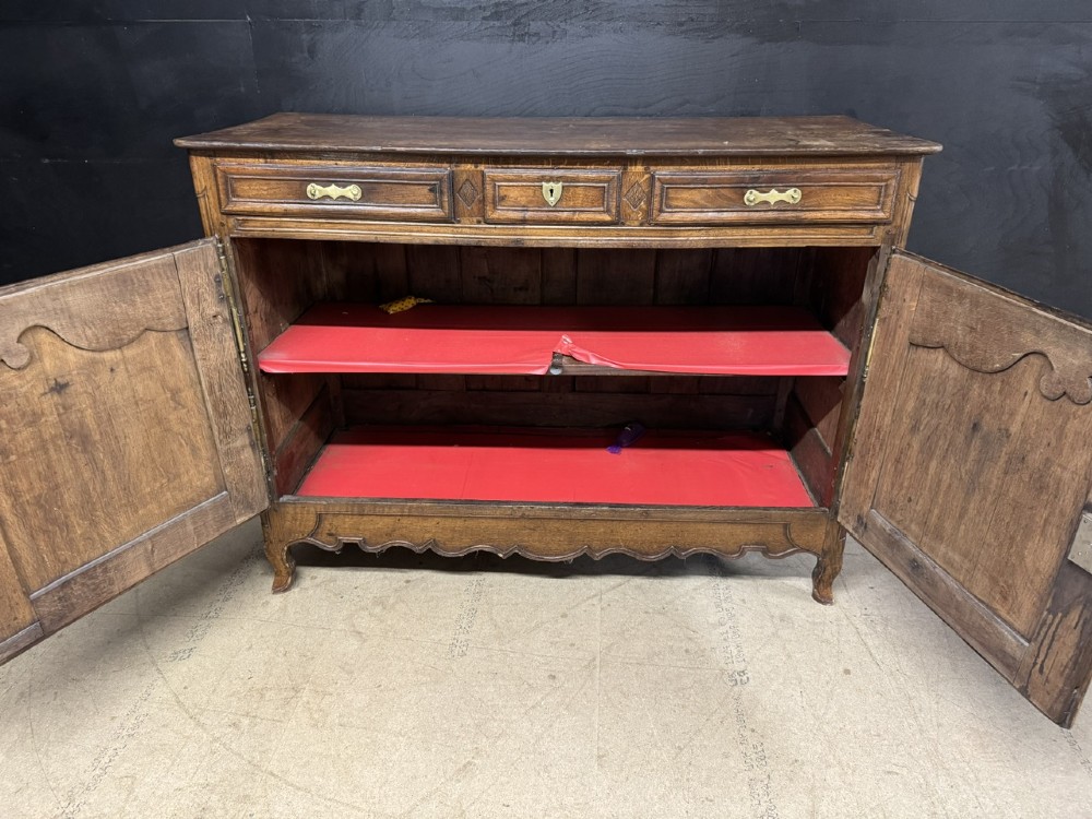 An 18th-century French provincial oak buffet featuring three top drawers above two carved panel doors with brass hardware. View IX