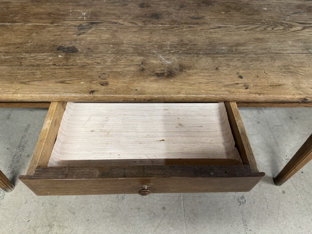 A rectangular natural oak French Normandy country table featuring a simple plank top, tapered legs, and a single frieze drawer. View VIII