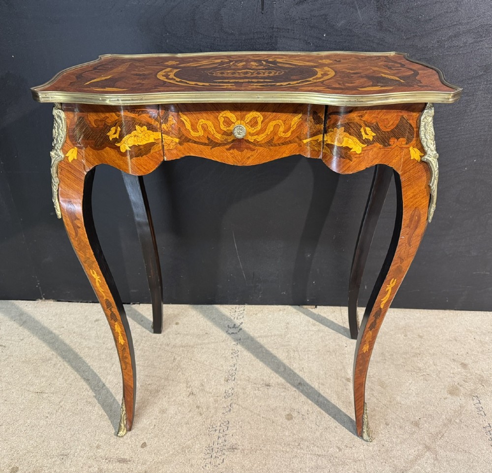 A French Louis XV style marquetry side table featuring cabriole legs, decorative brass mounts, and detailed floral wood inlay across the serpentine top and drawer.
