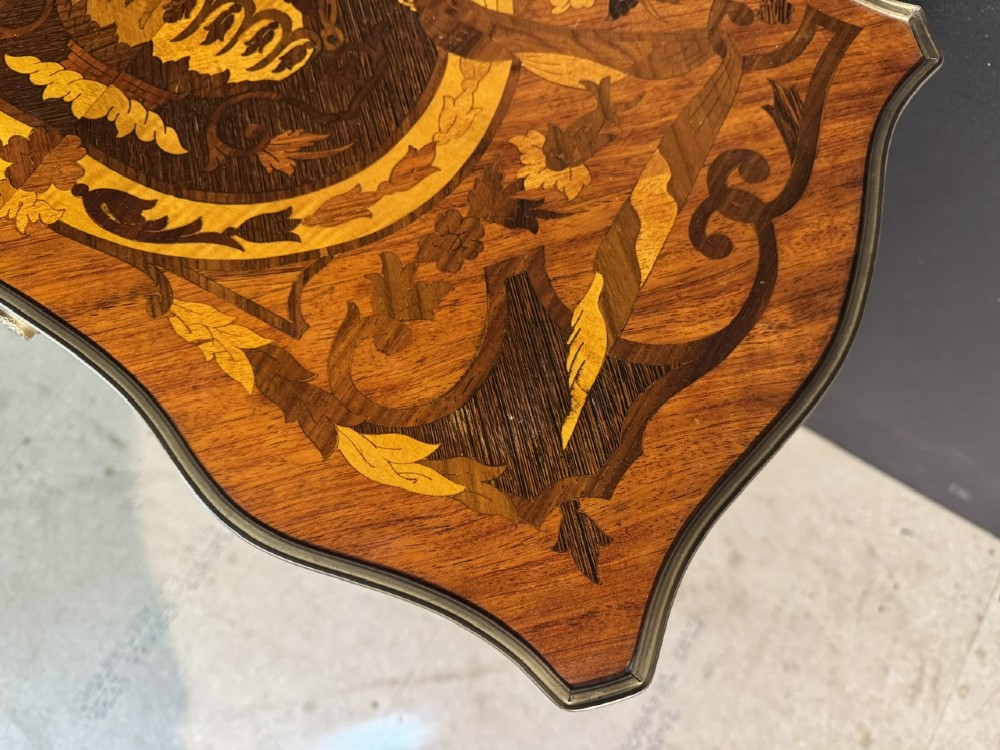 A French Louis XV style marquetry side table featuring cabriole legs, decorative brass mounts, and detailed floral wood inlay across the serpentine top and drawer. View XV