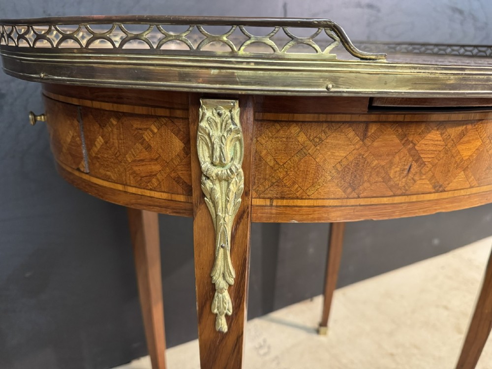 An oval French side table featuring a red veined marble top with a pierced brass gallery, geometric parquetry apron, and four tapered legs adorned with brass mounts. View VI