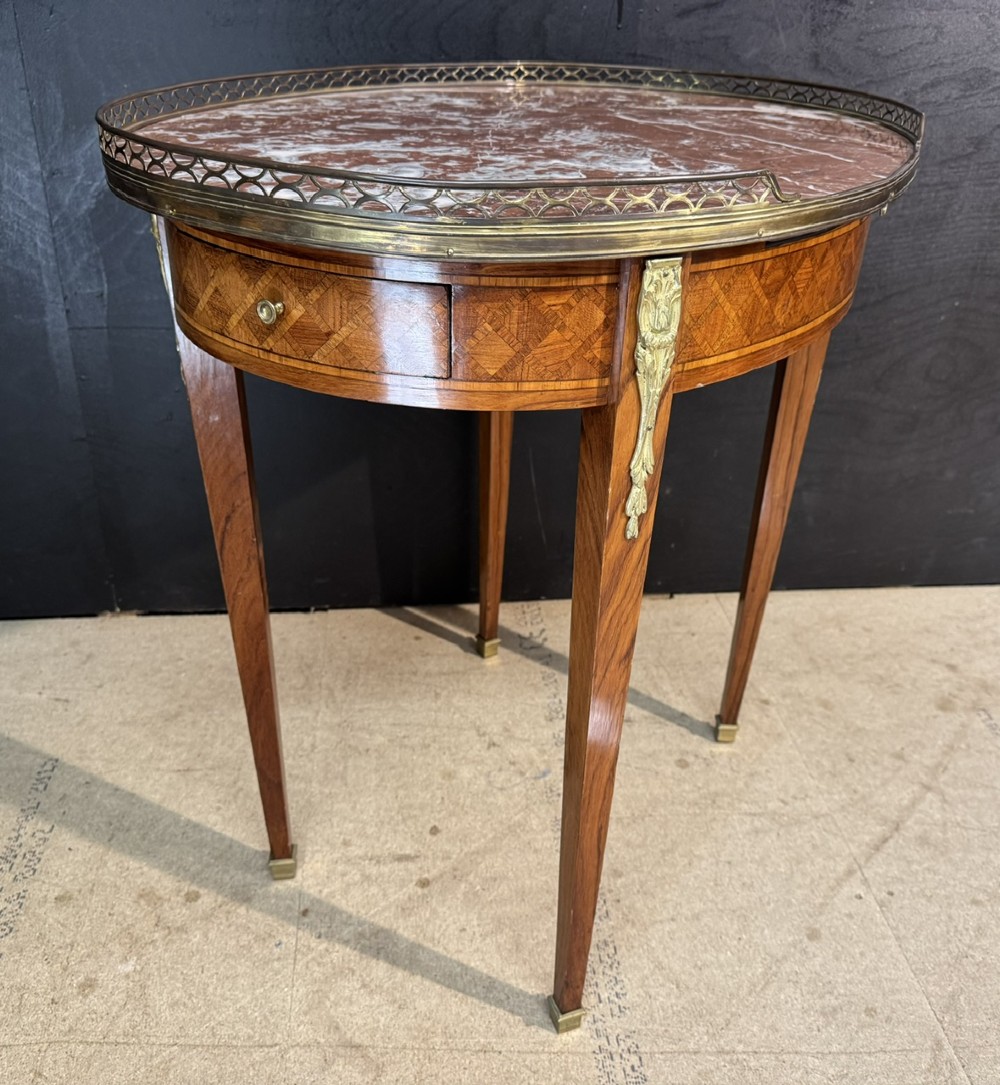An oval French side table featuring a red veined marble top with a pierced brass gallery, geometric parquetry apron, and four tapered legs adorned with brass mounts. View X