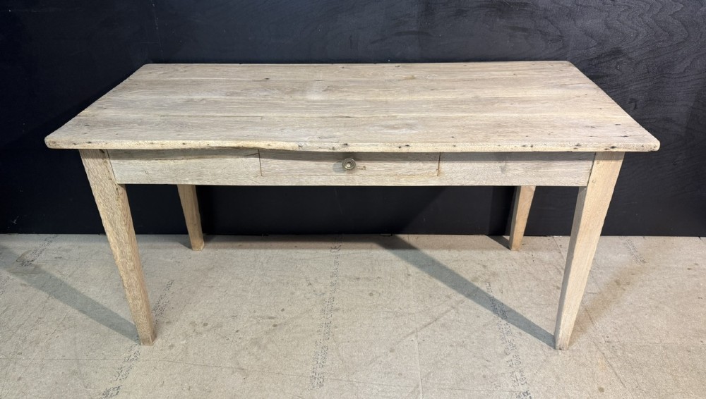 A rustic light oak French Normandy table featuring a flat plank top, a single central frieze drawer with a metal knob, and four square tapered legs.