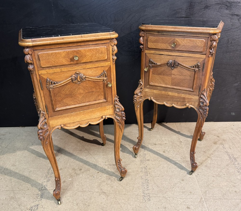 A pair of French walnut bedside cabinets with carved cabriole legs, dark marble tops, single drawers, and cupboard doors.