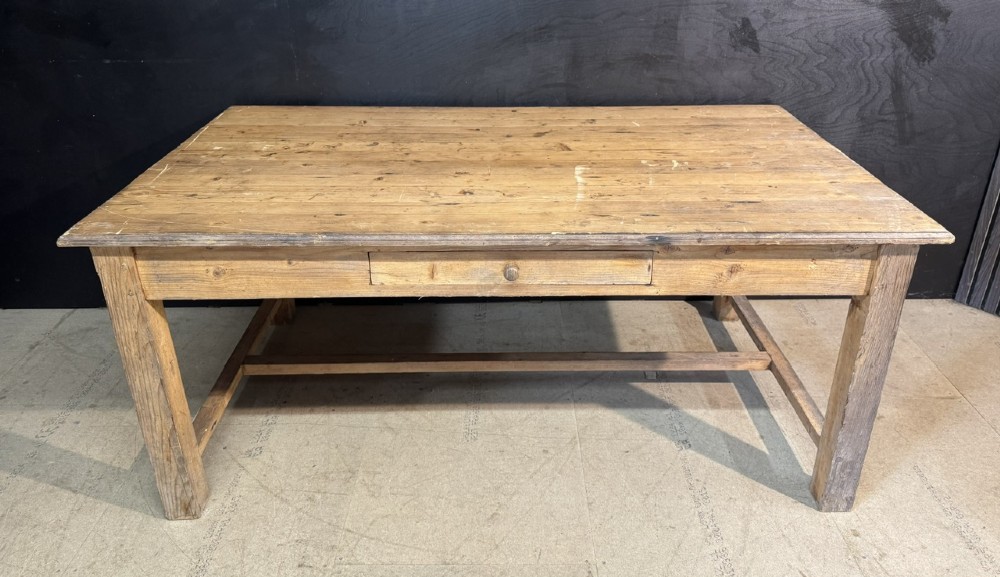 A rustic natural pine farmhouse kitchen table featuring a plank top, a single apron drawer, square legs, and a low stretcher base.