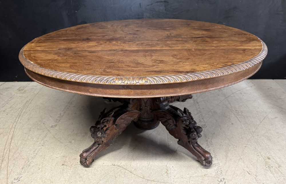 A round French carved oak dining table featuring a detailed rope-twist edge and a central pedestal base supported by four carved mythical figures.