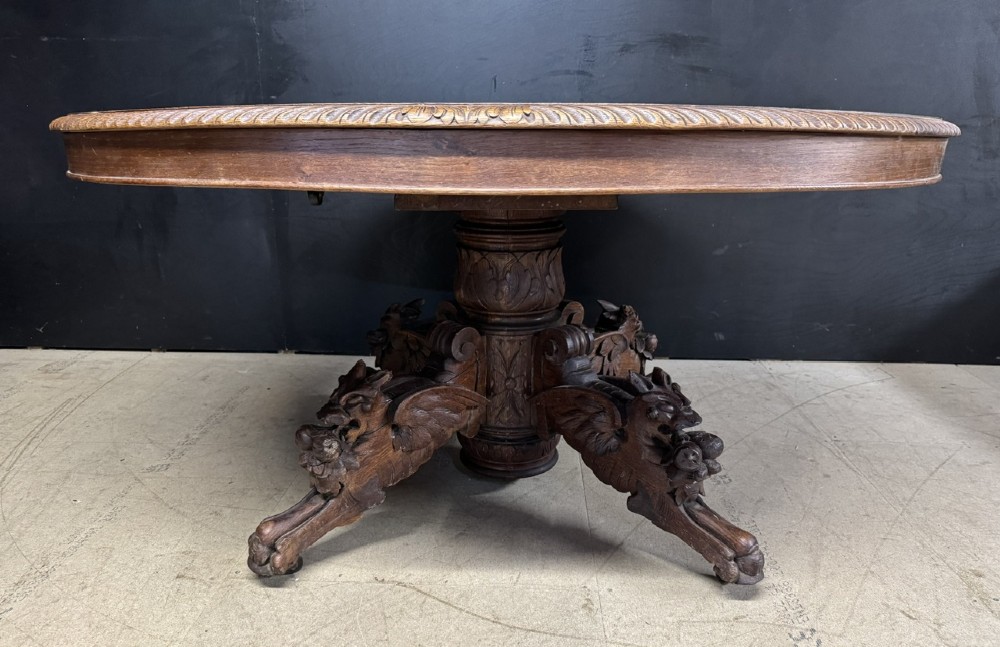 A round French carved oak dining table featuring a detailed rope-twist edge and a central pedestal base supported by four carved mythical figures. View II