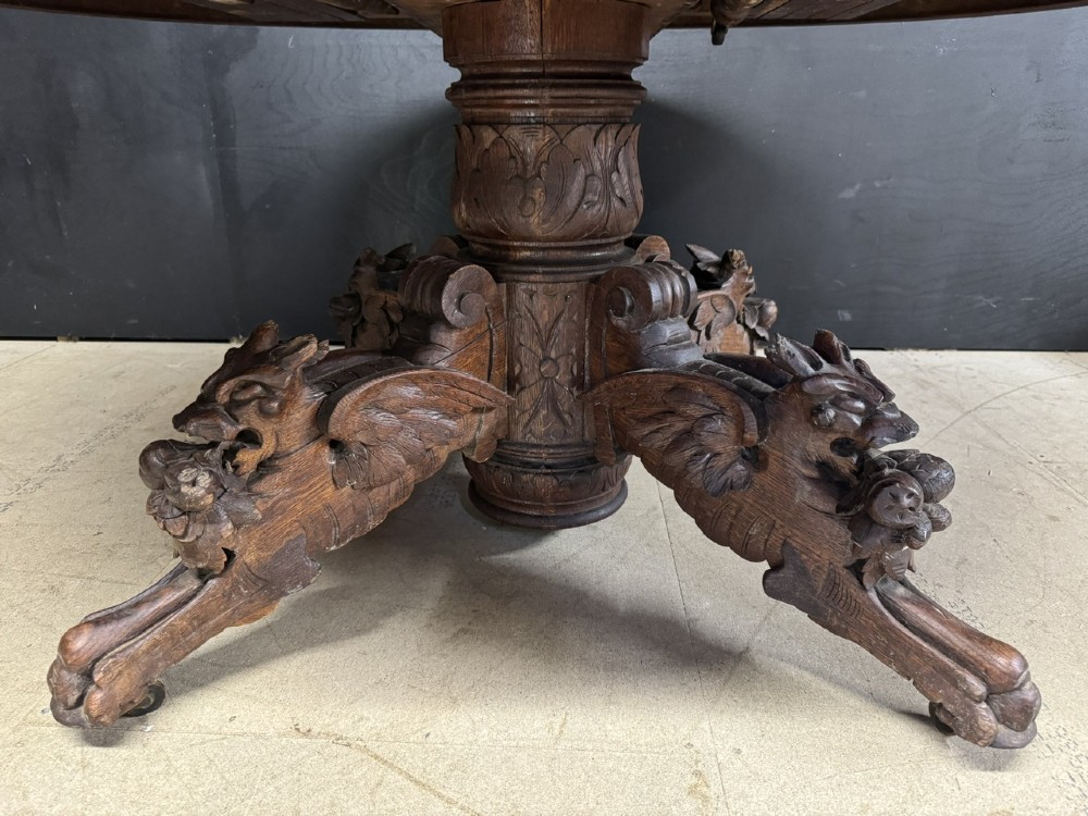 A round French carved oak dining table featuring a detailed rope-twist edge and a central pedestal base supported by four carved mythical figures. View III