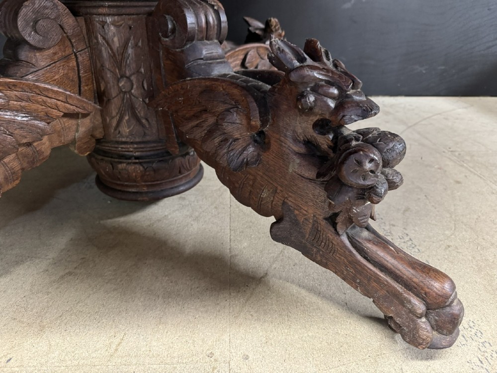 A round French carved oak dining table featuring a detailed rope-twist edge and a central pedestal base supported by four carved mythical figures. View IV