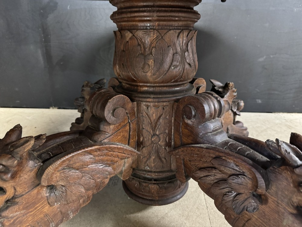 A round French carved oak dining table featuring a detailed rope-twist edge and a central pedestal base supported by four carved mythical figures. View V