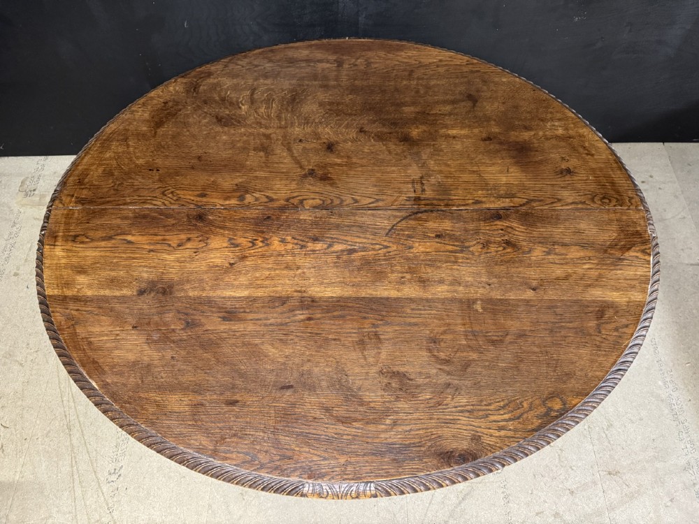 A round French carved oak dining table featuring a detailed rope-twist edge and a central pedestal base supported by four carved mythical figures. View VI