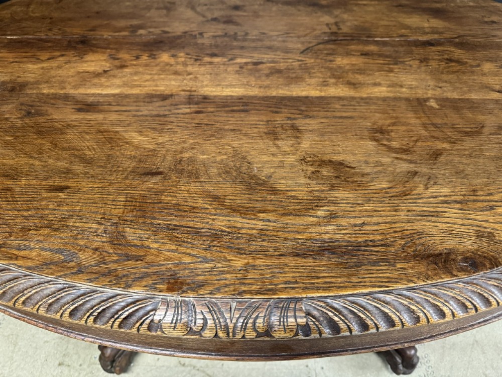 A round French carved oak dining table featuring a detailed rope-twist edge and a central pedestal base supported by four carved mythical figures. View VII