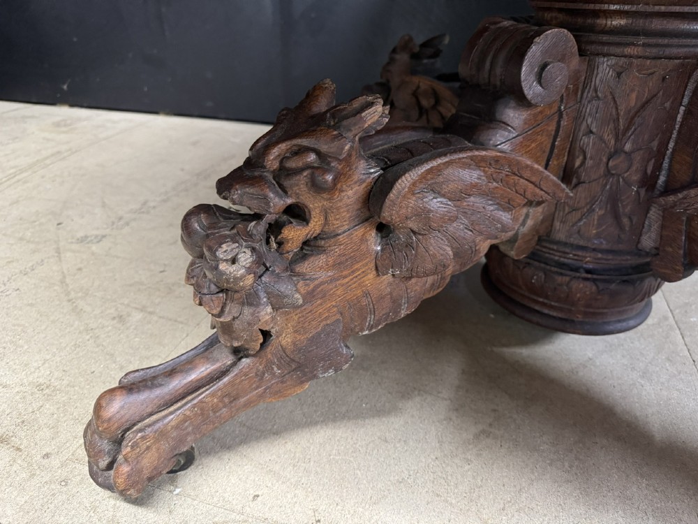 A round French carved oak dining table featuring a detailed rope-twist edge and a central pedestal base supported by four carved mythical figures. View VIII