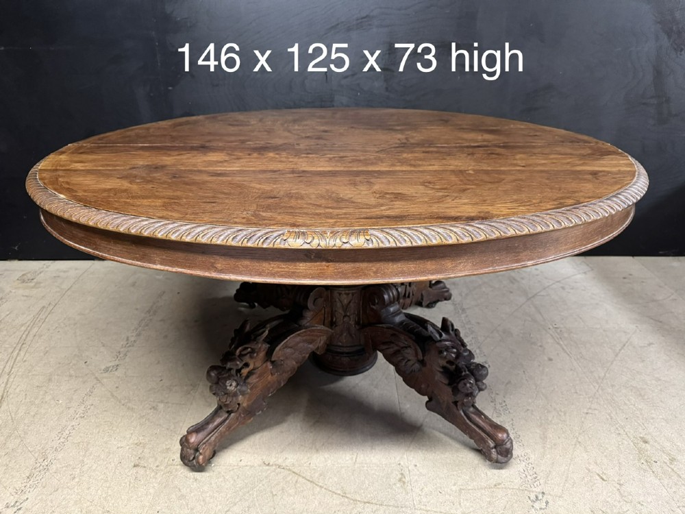 A round French carved oak dining table featuring a detailed rope-twist edge and a central pedestal base supported by four carved mythical figures. View IX