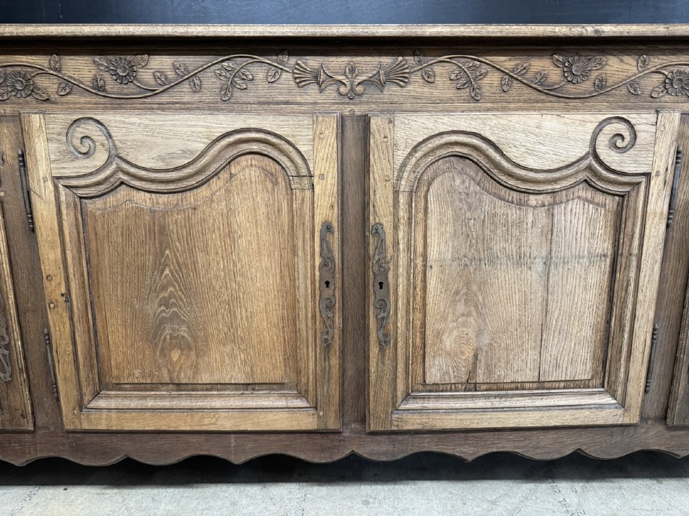 A long French oak enfilade featuring four cupboards with arched fielded panels, decorative floral carvings along the frieze, and two side drawers. View III