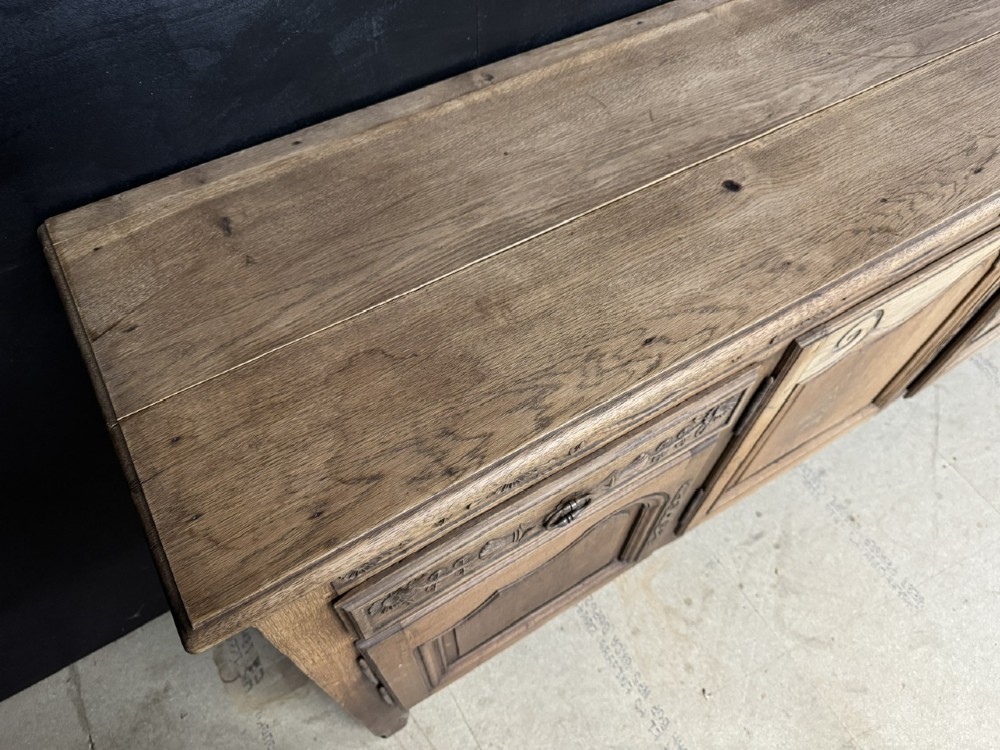 A long French oak enfilade featuring four cupboards with arched fielded panels, decorative floral carvings along the frieze, and two side drawers. View XIII