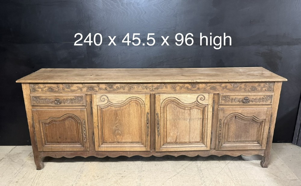 A long French oak enfilade featuring four cupboards with arched fielded panels, decorative floral carvings along the frieze, and two side drawers. View XIV