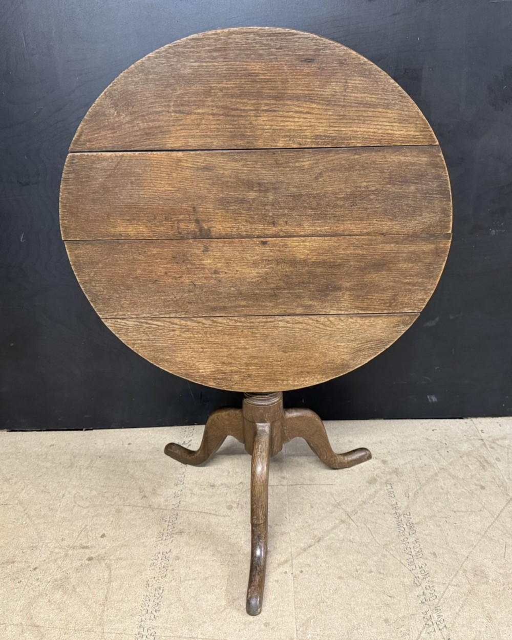 A circular Georgian oak tilt-top table positioned upright on a central turned column with three curved tripod legs.