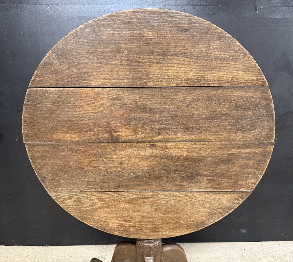 A circular Georgian oak tilt-top table positioned upright on a central turned column with three curved tripod legs. View II