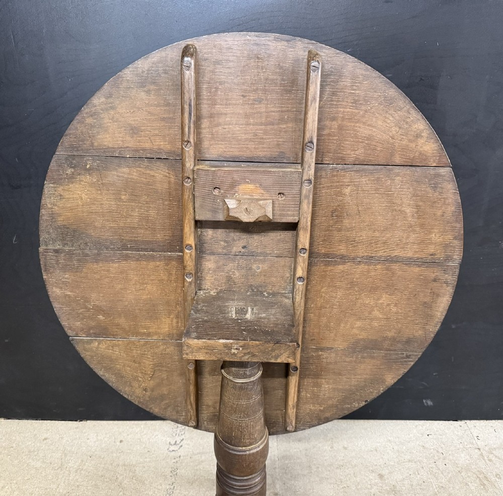 A circular Georgian oak tilt-top table positioned upright on a central turned column with three curved tripod legs. View IV