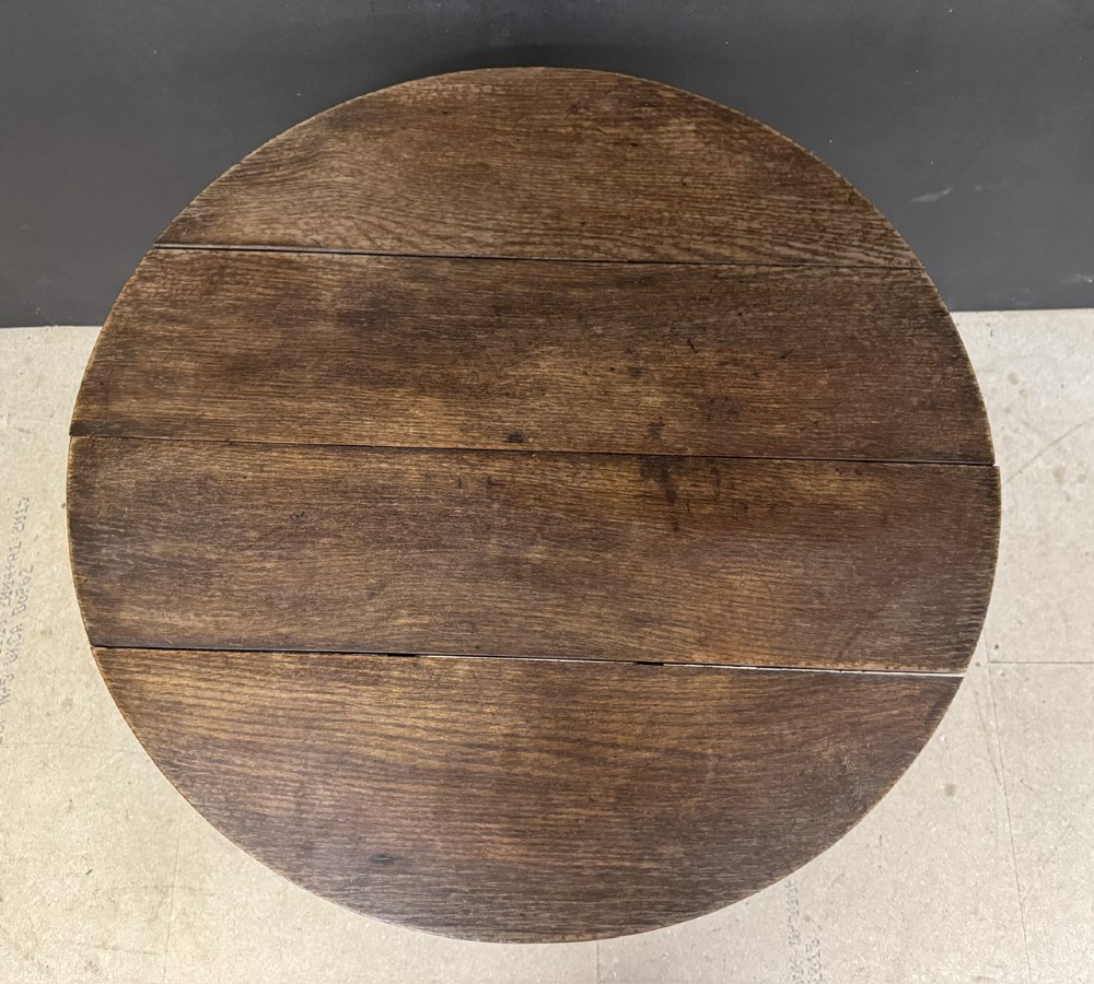 A circular Georgian oak tilt-top table positioned upright on a central turned column with three curved tripod legs. View V