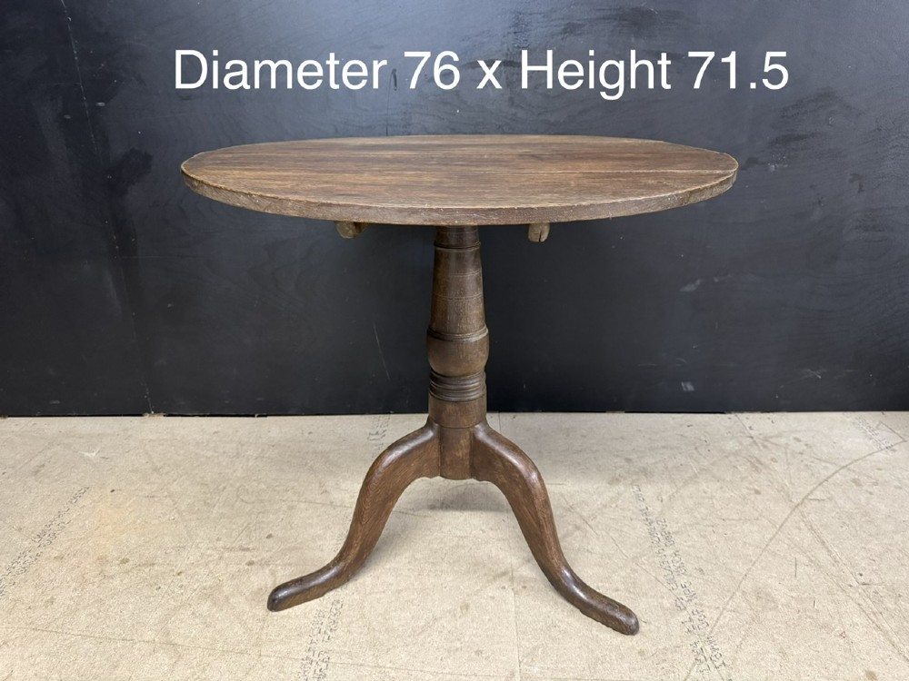 A circular Georgian oak tilt-top table positioned upright on a central turned column with three curved tripod legs. View VII