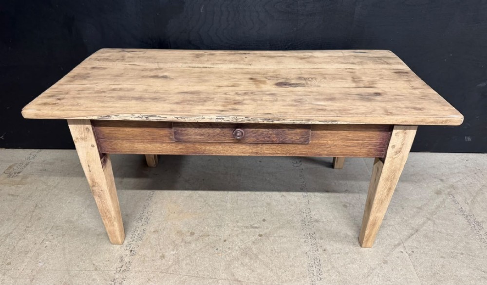 A low French oak coffee table with a rectangular light wood plank top, a single frieze drawer, and tapered square legs.