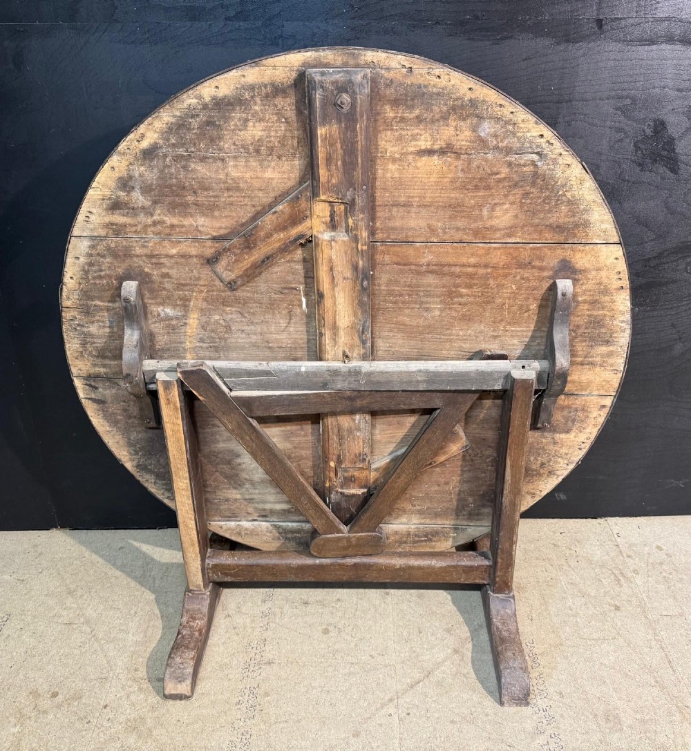 A circular rustic French wine tasting table made of pale planked timber tilted vertically on a wooden trestle base. View II