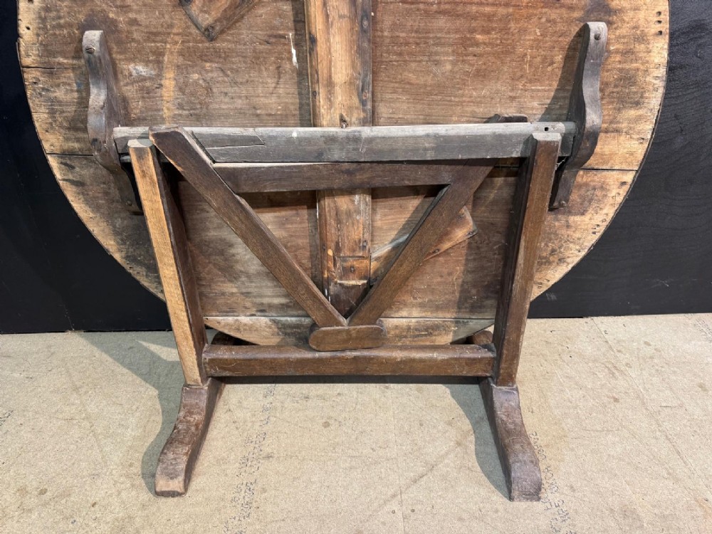A circular rustic French wine tasting table made of pale planked timber tilted vertically on a wooden trestle base. View III