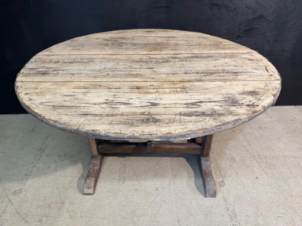A circular rustic French wine tasting table made of pale planked timber tilted vertically on a wooden trestle base. View IV