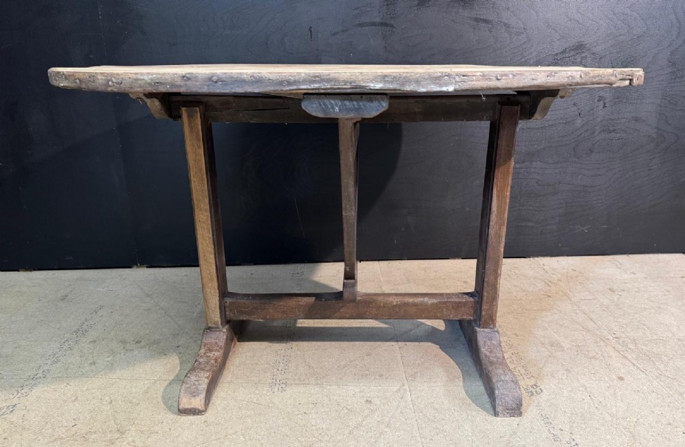A circular rustic French wine tasting table made of pale planked timber tilted vertically on a wooden trestle base. View V