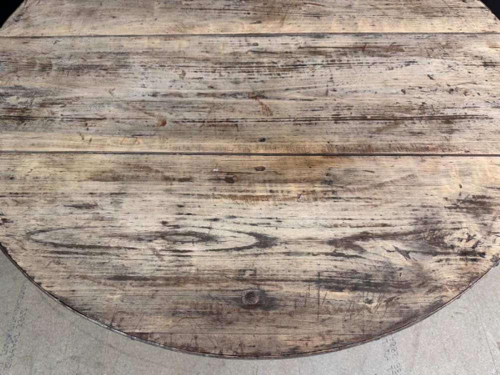 A circular rustic French wine tasting table made of pale planked timber tilted vertically on a wooden trestle base. View VI