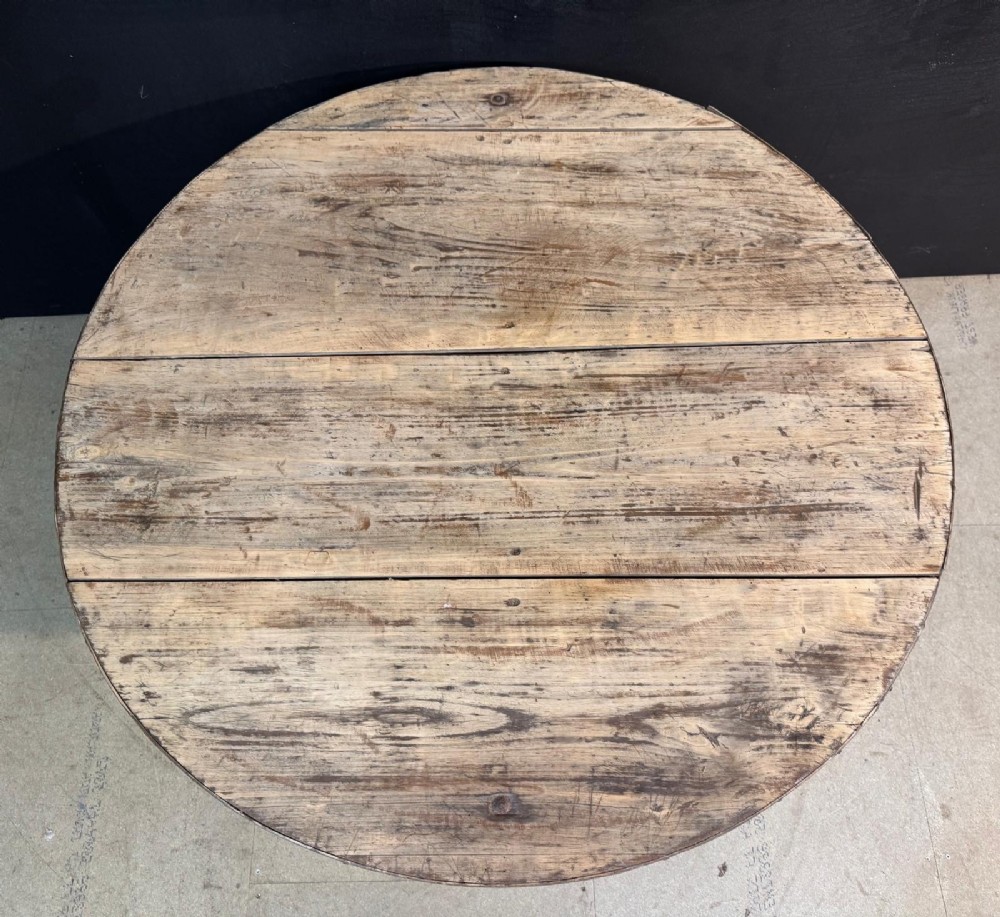 A circular rustic French wine tasting table made of pale planked timber tilted vertically on a wooden trestle base. View VII