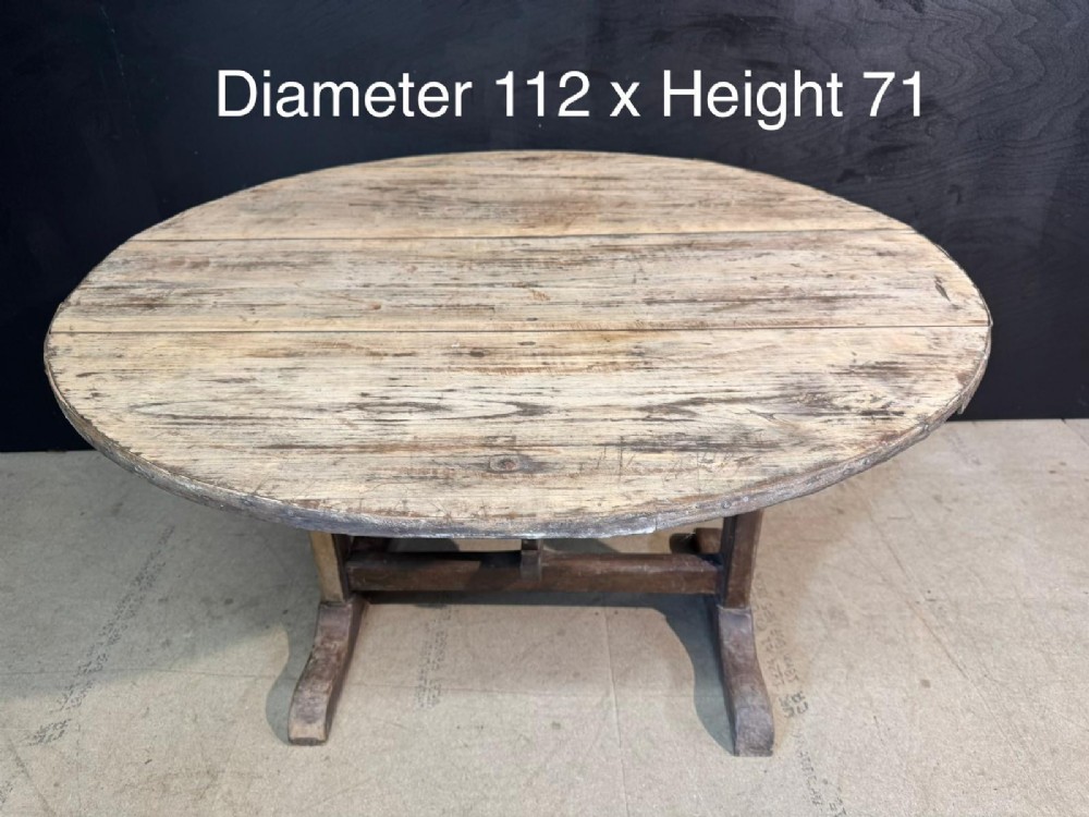 A circular rustic French wine tasting table made of pale planked timber tilted vertically on a wooden trestle base. View XII